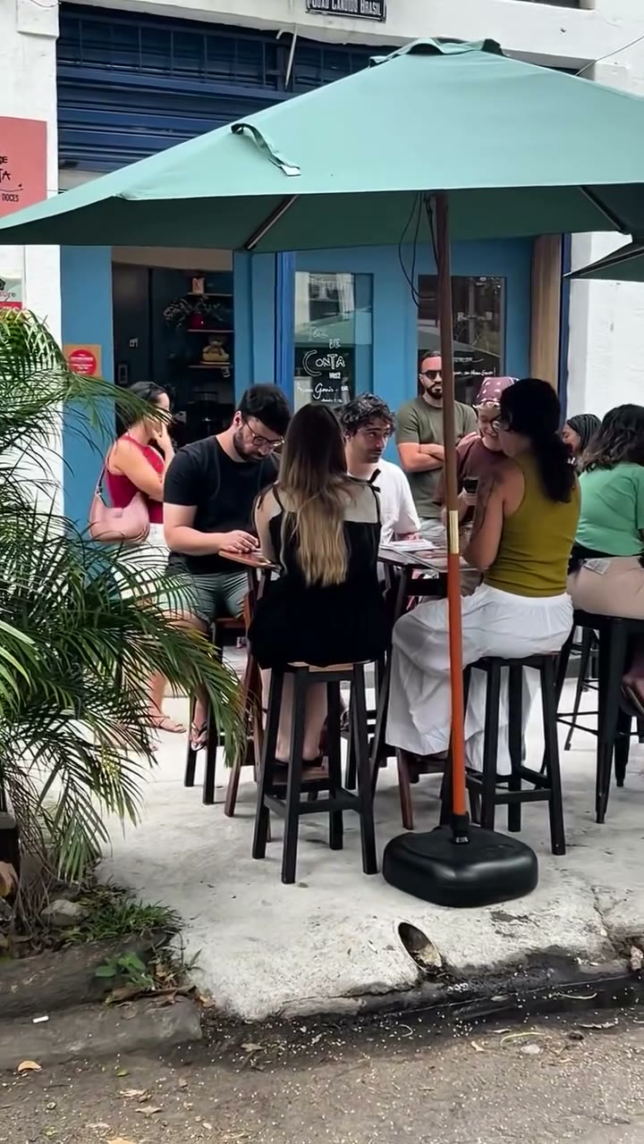 Clientes nas mesas da calçada, sob o guarda-sol